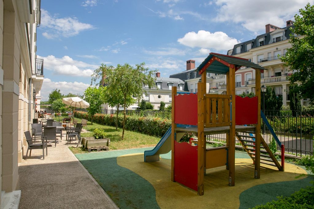 Terrasses fermée par une barrière avec tables, parasoles et toboggan pour les enfants