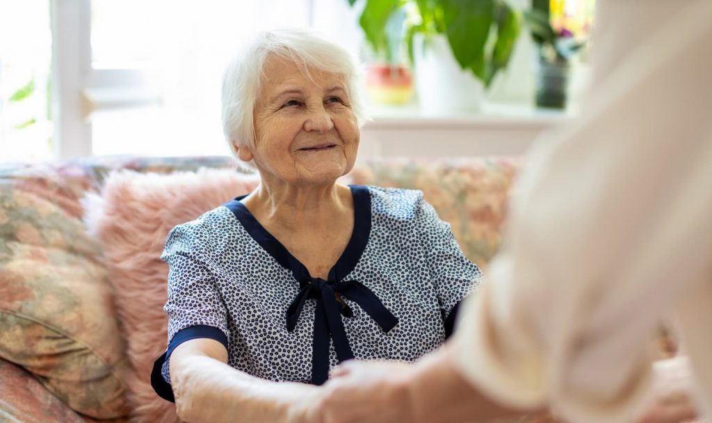 Personne âgée sur son canapé tient les mains d'une aidante