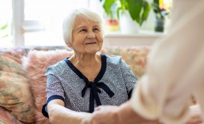 Personne âgée sur son canapé tient les mains d'une aidante